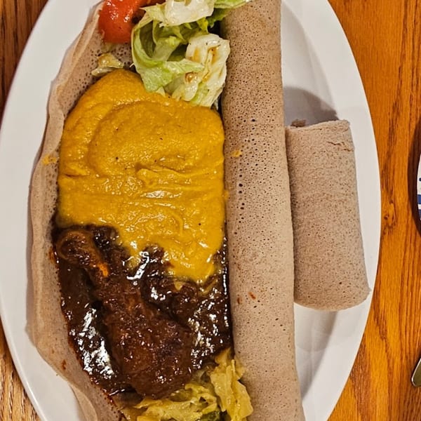 Ethiopian injera bread with yellow shiro, dark stew, and a side salad on a white plate.