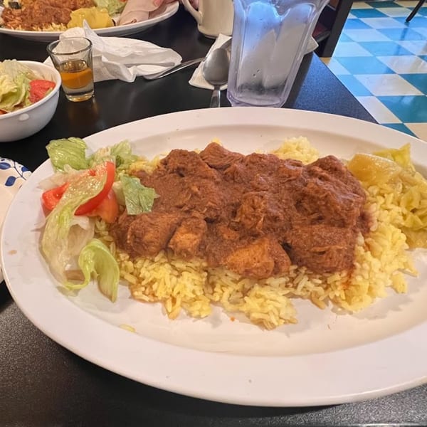 Altu's Ethiopian Cuisine's chicken stew with yellow rice, salad, and a shot glass of amber liquid.