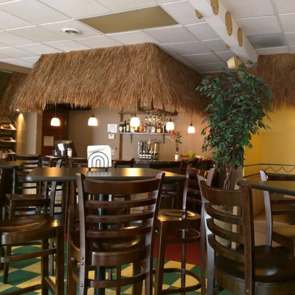 Interior of Altu's Ethiopian Cuisine with a thatched roof bar, tables, chairs, and checkered floor.
