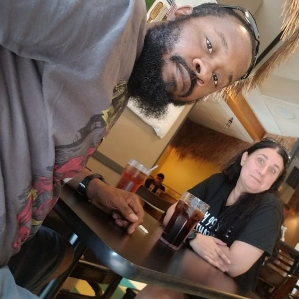 A man takes a selfie with a woman sitting across from him at a table in Altu's Ethiopian Cuisine.