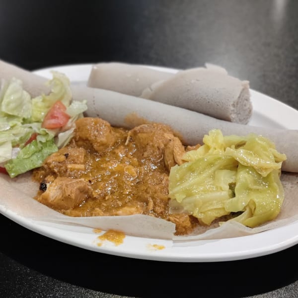 Ethiopian injera bread with chicken stew, cabbage, and a side salad on a white plate.