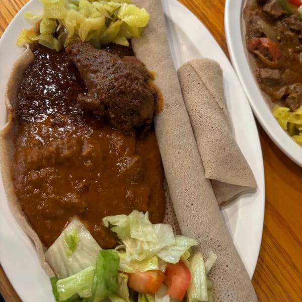 Ethiopian injera bread with a rich stew, cabbage, and a side salad on a white plate.