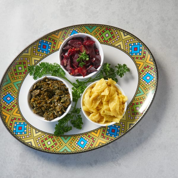 Three bowls of Ethiopian dishes: red beets, green collard greens, and yellow cabbage, on a colorful platter.